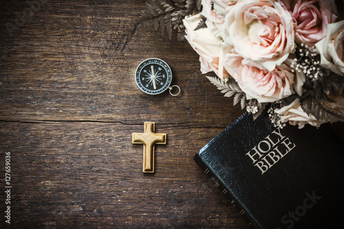 the wooden cross with compass and holy bible and roses flowers on wooden background, vintage tone and effect photo