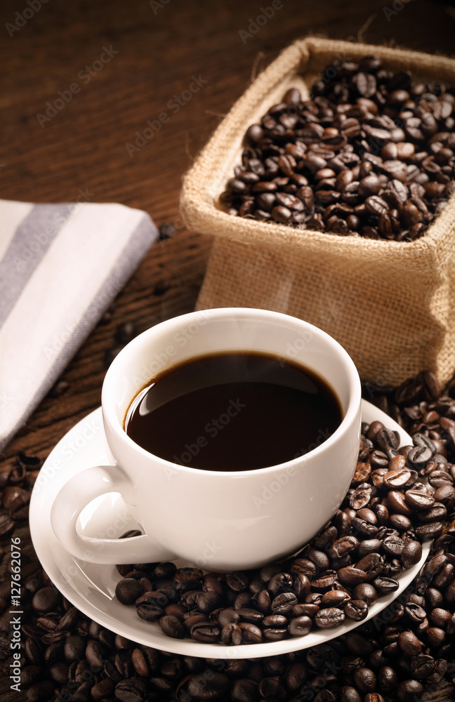 Fototapeta premium warm cup of coffee with sack inside by coffee bean on wood background