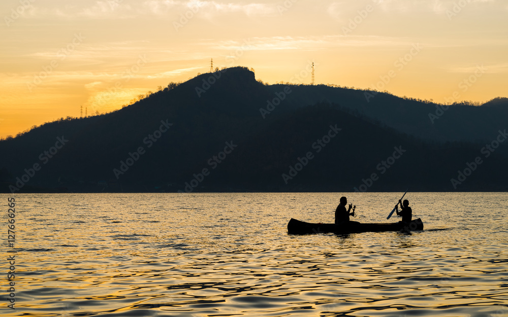 silhouette of two men are boating in the dam on the morning.