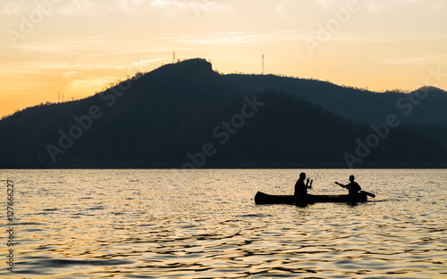 silhouette of two men are boating in the dam on the morning.