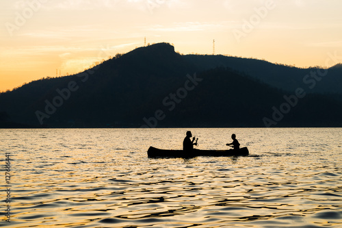 silhouette of two men are boating in the dam on the morning.