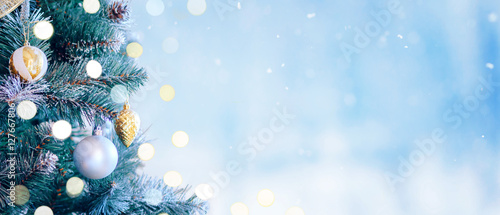 Decorated Christmas tree with bright bokeh on winter blue snowy background. Christmas border. 