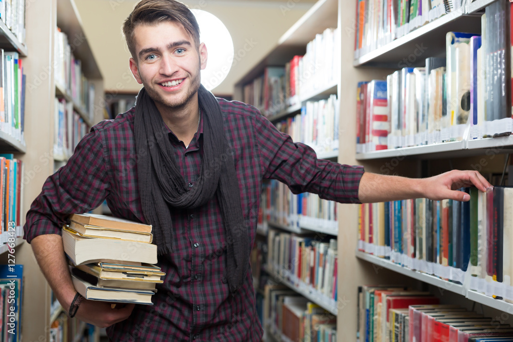 Smiling male student picking a book in a library Smiling male student picking a book in a library