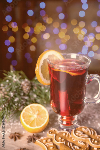 Mulled wine with lemon and cinamon sticks in glass and christmas cookies on the wooden table with christmas tree branch and snow