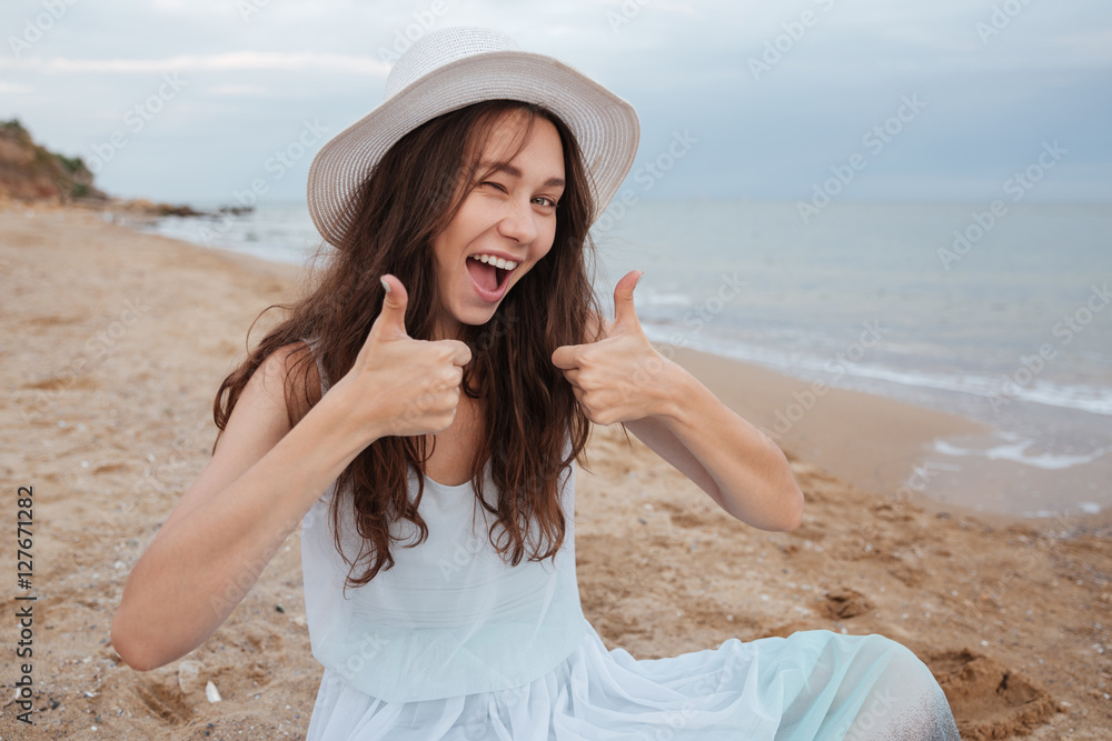 Cheerful woman winking and showing thumbs up on the beach Cheerful woman winking and showing thumbs up on the beach
