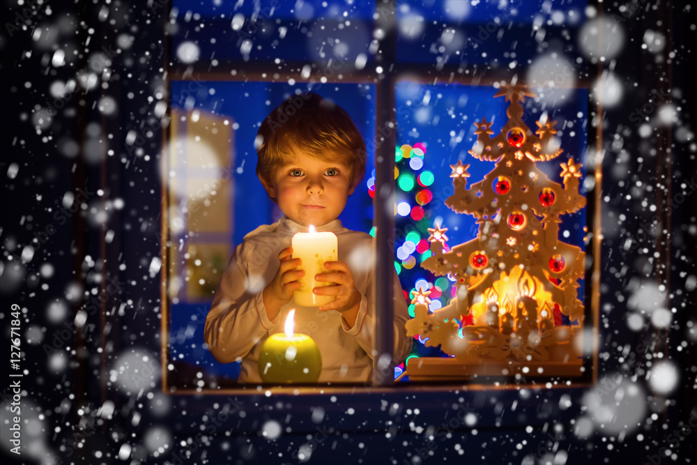 Little kid boy standing by window at Christmas time and holding Little kid boy standing by window at Christmas time and holding