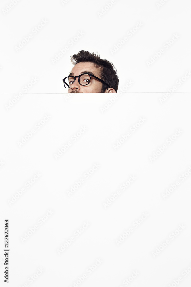 Portrait of man peering over white surface in studio