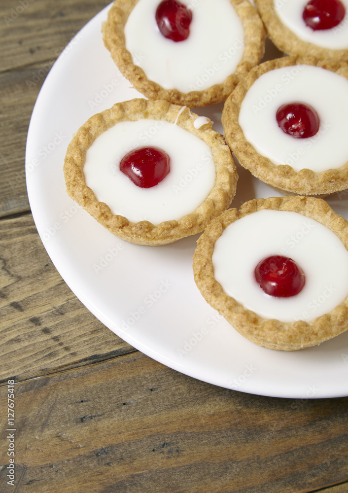 A plate full of freshly baked Bakewell tarts on a rustic wooden table top background A plate full of freshly baked Bakewell tarts on a rustic wooden table top background