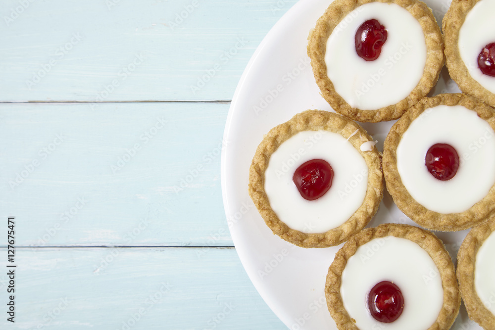 Aerial view of a plate full of freshly baked Bakewell tarts on a blue wooden table top background with blank space at side Aerial view of a plate full of freshly baked Bakewell tarts on a blue wooden table top background with blank space at side