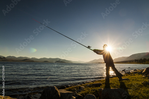 Silhouette of a fisherman at sunset. Fishing on mountain lake photo