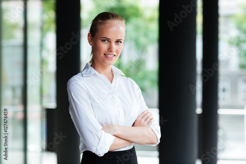 Happy pretty young businesswoman standing with arms crossed
