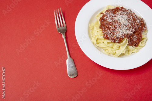 A dinner dish of spaghetti Bolognese on a bright red background with fork and blank space at side