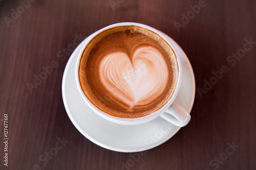 In a special atmosphere, cup of hot, soft latte art with heart on the wooden table in the cafe.