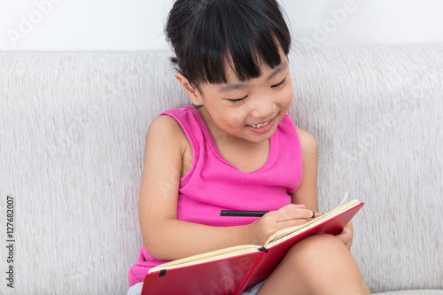 Happy Asian Chinese little girl sitting on sofa writting book