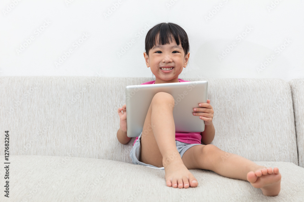 Happy Asian Chinese little girl sitting on sofa with tablet Happy Asian Chinese little girl sitting on sofa with tablet