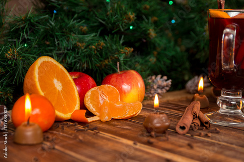 Candles, fruits and spices on wooden table near mulled wine. Christmas decorations in background. New year.