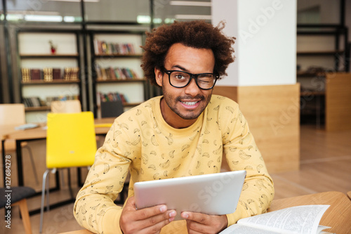 Happy african man in glasses with tablet in library