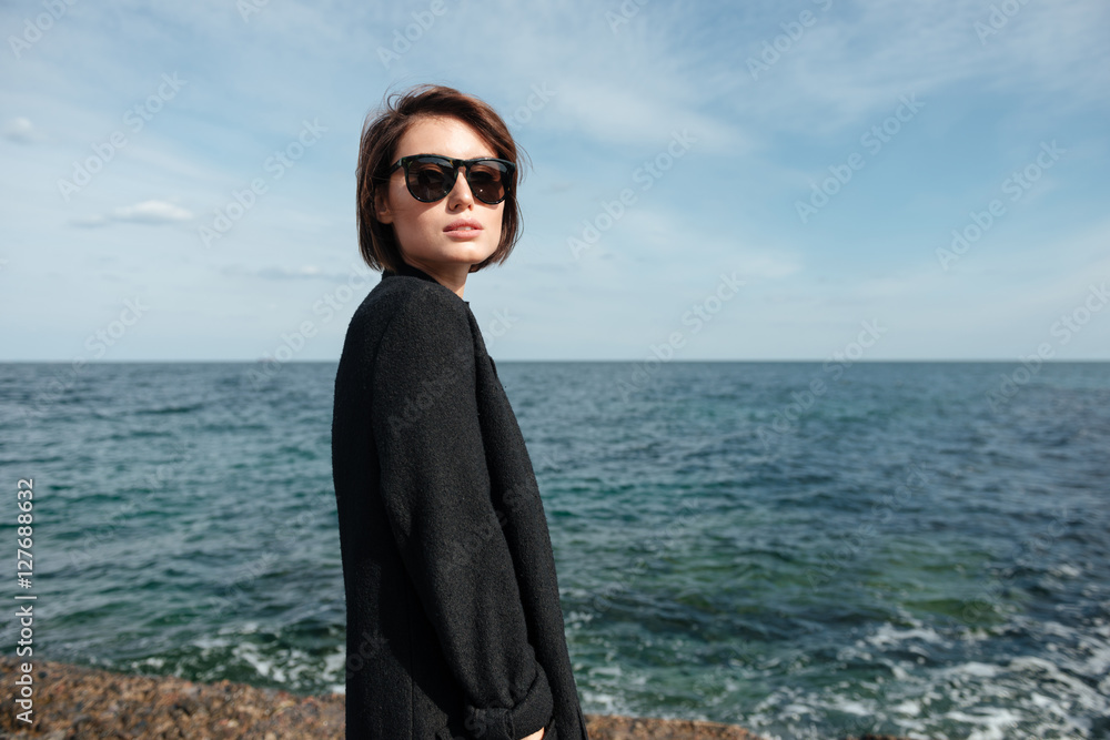 Woman in sunglasses and black coat on the seaside Woman in sunglasses and black coat on the seaside
