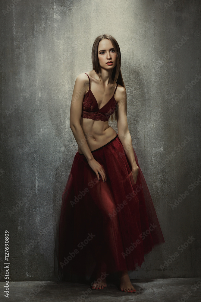Fototapeta Portrait of slim young girl dancer in red long skirt that sits o