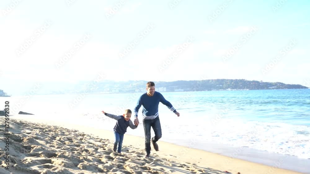 Father and son running on a sandy beach in autumn Father and son running on a sandy beach in autumn
