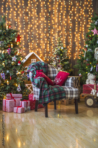 Новогодние декорации с креслом, клетчатым пледом, красными подушками, подарками, новогодней елкой, украшенной новогодними игрушками и свечами, пряничным домиком, тележкой, гирляндой с желтыми огнями