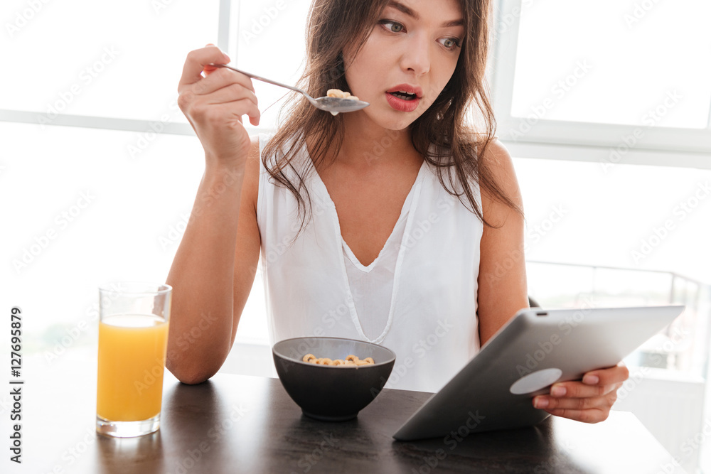Amazed woman having breakfast and using tablet on the kitchen Amazed woman having breakfast and using tablet on the kitchen
