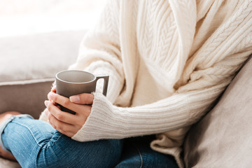 Woman with cup of coffee sitting on sofa at home