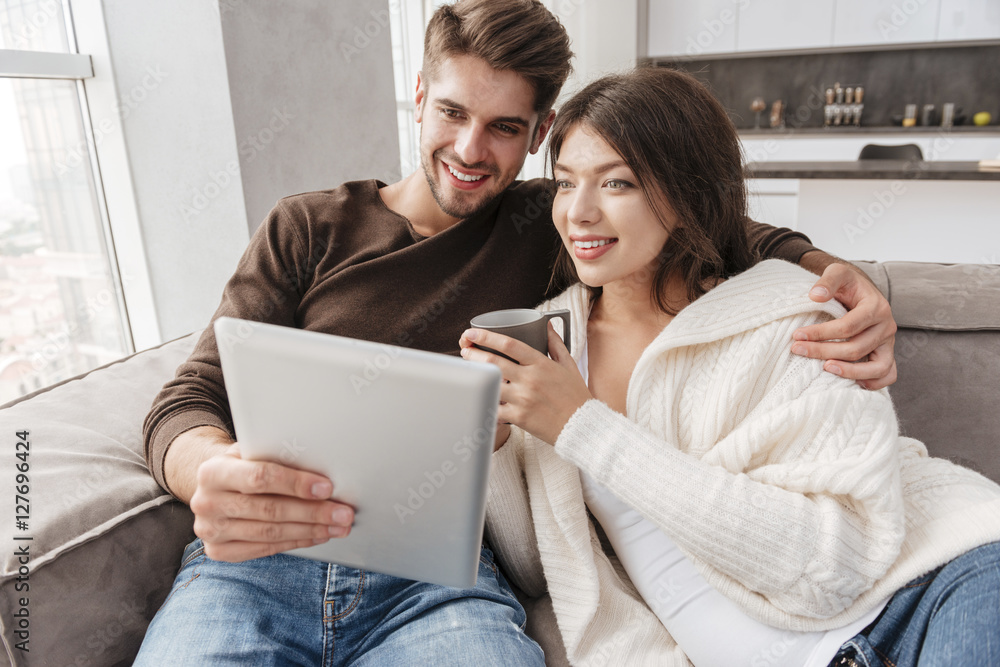 Happy couple drinking coffee and using tablet on sofa together Happy couple drinking coffee and using tablet on sofa together