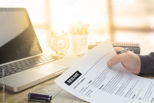 Businessman or job seeker review his resume on his desk before send to finding a new job with pen, necktie, glasses and digital tablet.
