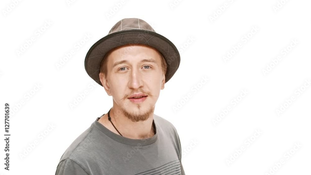 Displeased young handsome man in hat passing by over white background. Slow motion. Displeased young handsome man in hat passing by over white background. Slow motion.