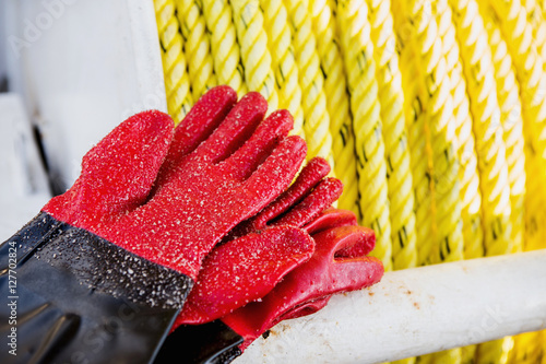 fishing gloves covered with sand lie on the boat. Fishing ship, fishing. Gloves red. Next to rubber gloves and rope lifeline. photo