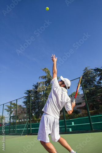 Professional tennis player is doing a kick tennis on a tennis court on a sunny summer morning. The is dressed in sportswear. 