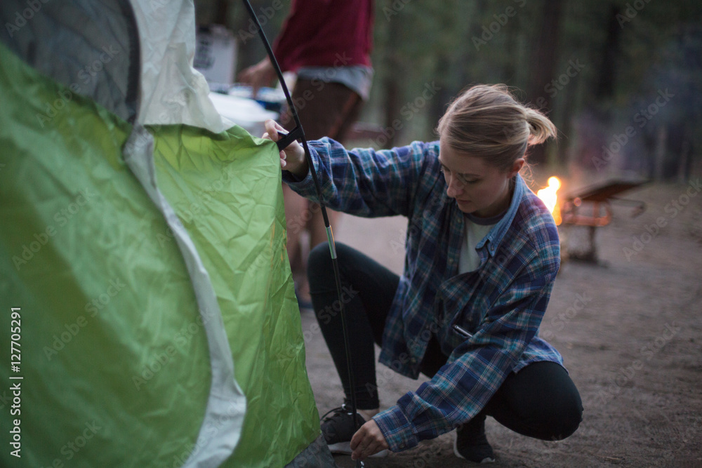 Young woman crouching to prepare tent at dusk, Mammoth Lakes, California, USA Young woman crouching to prepare tent at dusk, Mammoth Lakes, California, USA