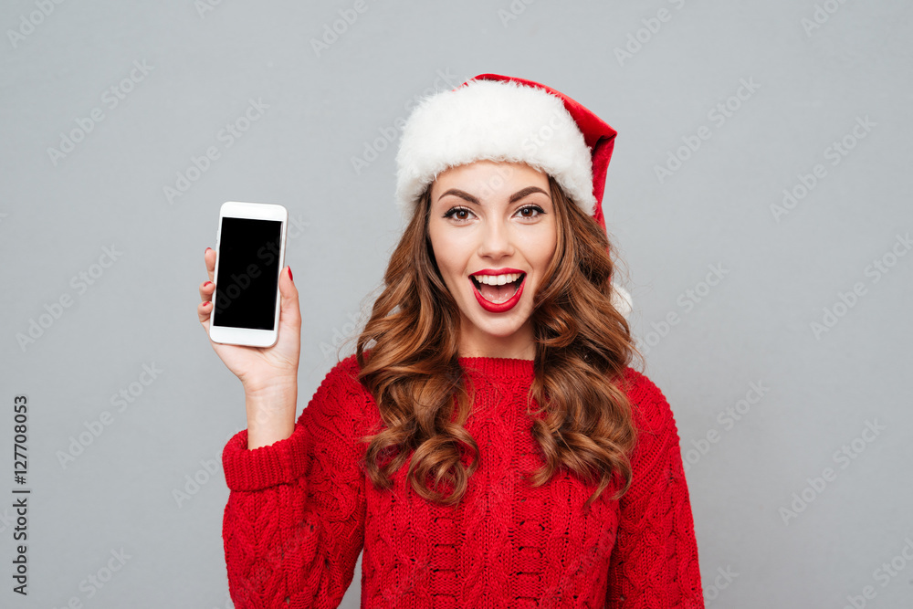 Smiling woman in santa claus hat showing blank screen smartphone Smiling woman in santa claus hat showing blank screen smartphone