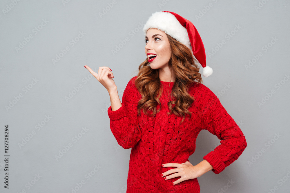 Cheerful woman in santa claus hat standing and pointing away Cheerful woman in santa claus hat standing and pointing away