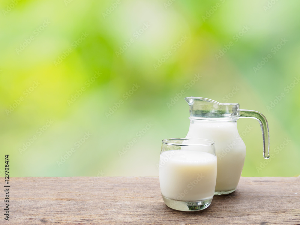 Milk jug and glass on wooden table of natural background Milk jug and glass on wooden table of natural background