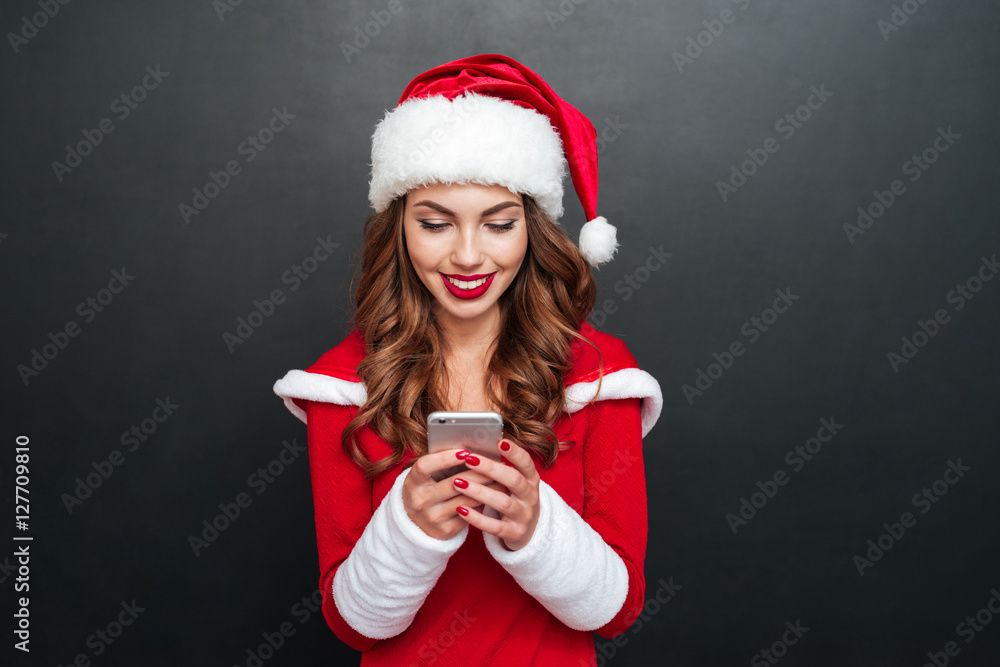 Smiling beautiful woman in santa claus hat using mobile phone Smiling beautiful woman in santa claus hat using mobile phone