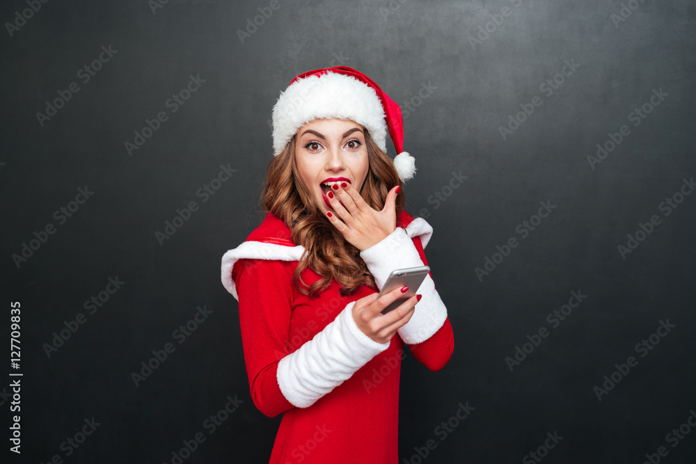 Surprised young woman in santa hat using mobile phone Surprised young woman in santa hat using mobile phone
