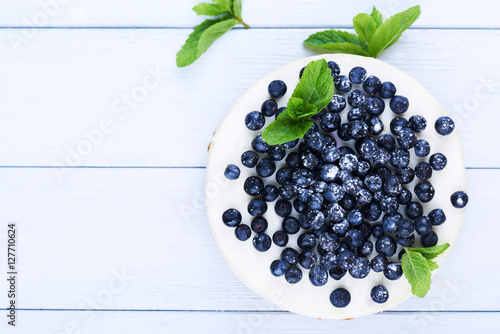 Sweet creamy blueberry cheesecake with fresh blueberries and mint leaves on a white wooden background with copy space.