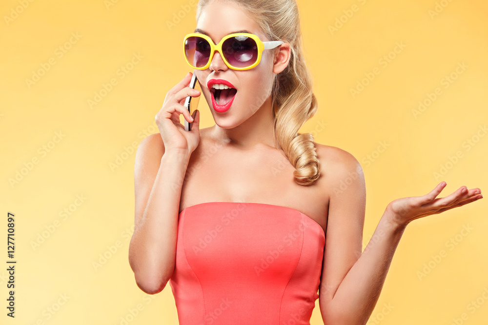 Fototapeta premium Young smiling woman talking by mobile phone about sale on black friday. Girl with yellow background and copy space