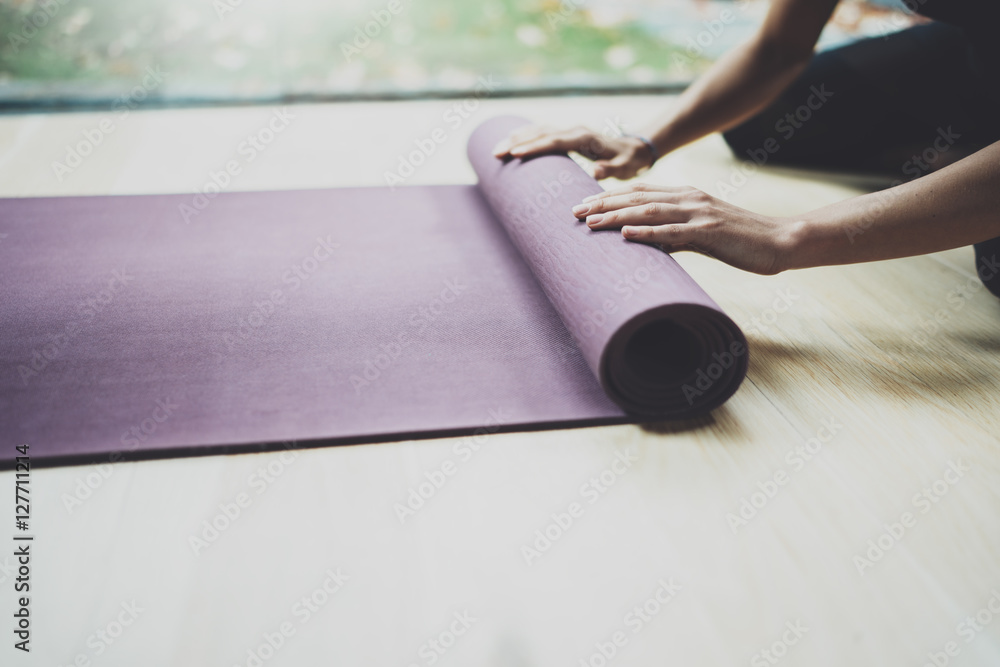 Close up view of gorgeous young woman practicing yoga indoor. Beautiful girl preparing mats with hands for practice class.Calmness and relax, female happiness concept.Horizontal, blurred background.
