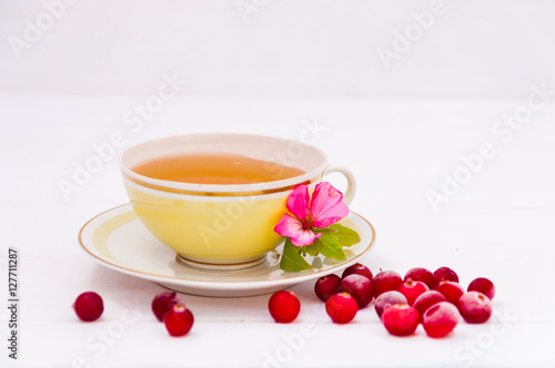 Yellow cup of tea and cranberries on white background