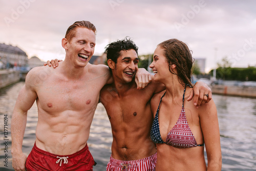 Young friends in swimwear standing together by the lake