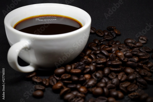 Closeup coffee beans and white ceramic coffee mug on the dark background.
