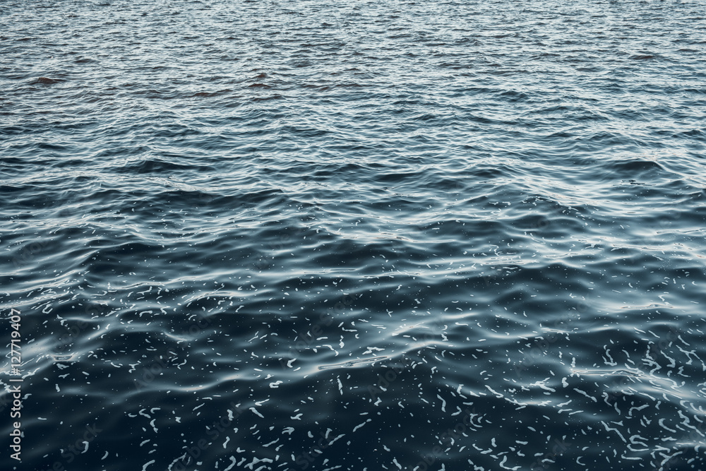 Obraz premium Sea surface aerial view. Background shot of clear sea water surface. Blue sea water in calm. Sea texture. Background blue waves of the sea with sea foam.