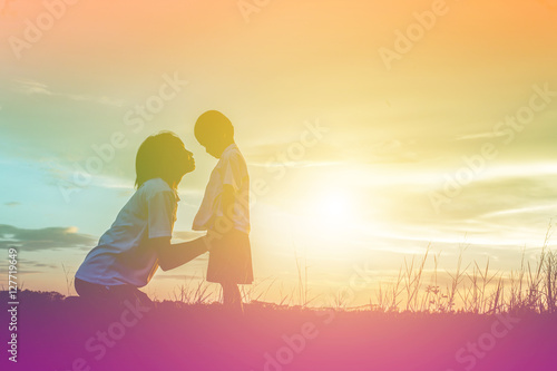 Silhouettes of mother and little daughter walking at sunset