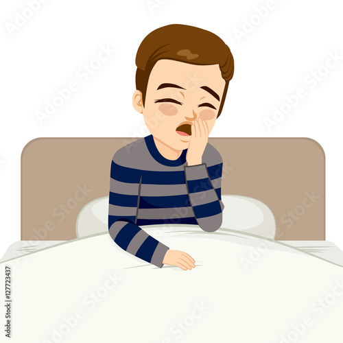 Young man waking up and yawning sitting on bed