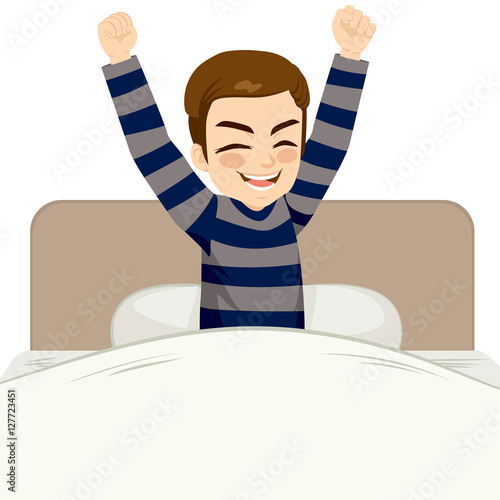 Young man happy waking up sitting on bed with arms up