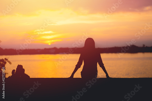Silhouette of woman sitting riverside and beautiful sunset background.