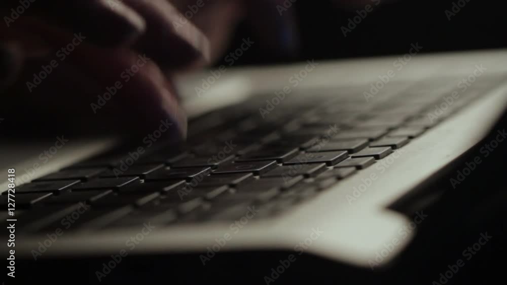 Close up of a Caucasian woman hands typing on the black keys of a silver notebook under low light Close up of a Caucasian woman hands typing on the black keys of a silver notebook under low light
